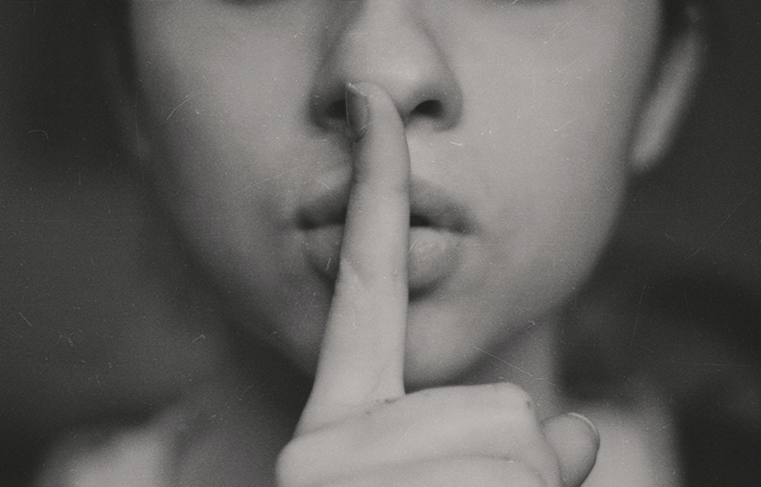 Fotografía en blanco y negro de alguien llevandose el dedo a los labios, mandando callar.